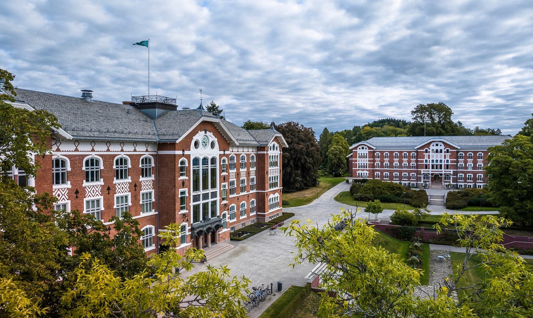 Majestetisk universitetsbygning i stein ved campusen i Ås, omgitt av et grønt og velstelt uteområde